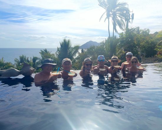 Casa de Sofia guests in the infinity pool with the water, palm trees and mountains behind