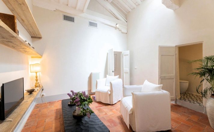 Another lounge area at Bella Aura, this one with two comfy white chairs, a low-slung coffee table, and wooden shelves with a flatscreen TV