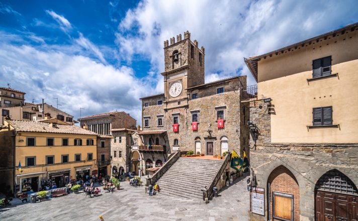 Street view of Cortona, showing beautiful stucco and stonework buildings, and large stone steps up to a main building.